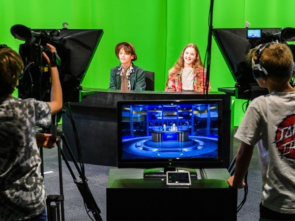 Children dressed as reporters being filmed in front of green screen.
