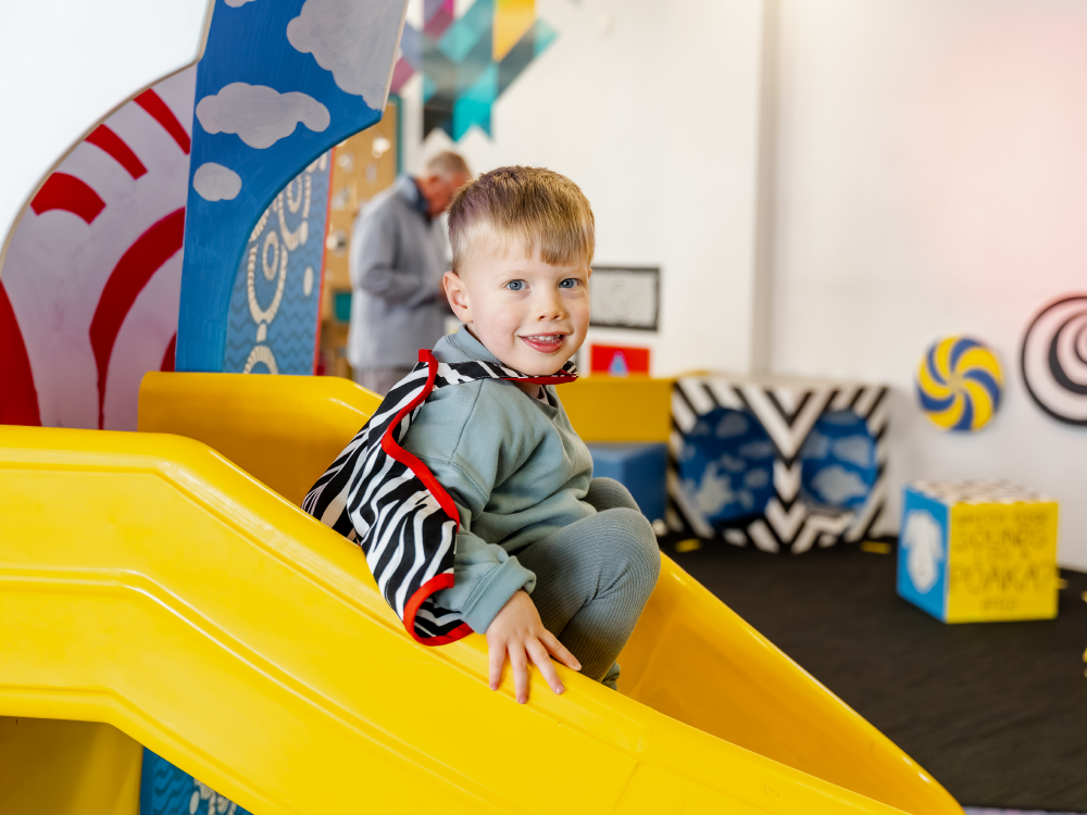 A child in PlayHQ, wearing a costume and sitting on the slide