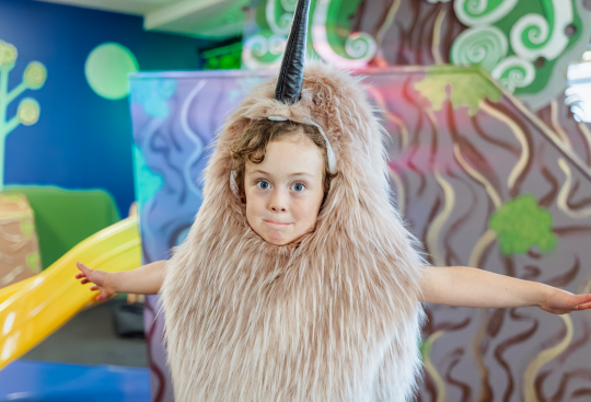 A child in a kiwi costume stands in front of a slide
