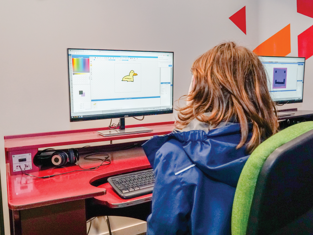 A child sits at a computer doing Advanced Game Design during the school holidays